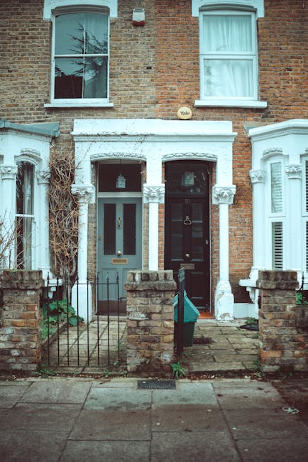 Photograph of two adjoining terraced houses with brick exteriors, located on a residential street. The left house features a green front door with a small window, and its porch area is partially enclo